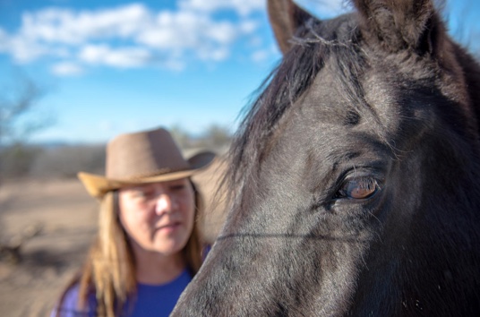 Susan in a cowboy hat beside a black horse